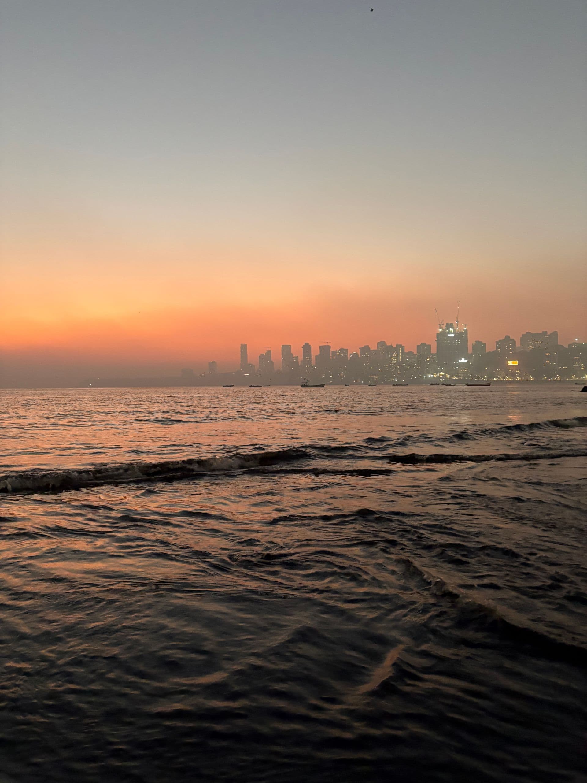 Mumbai skyline across the sea under an orange dusk sky